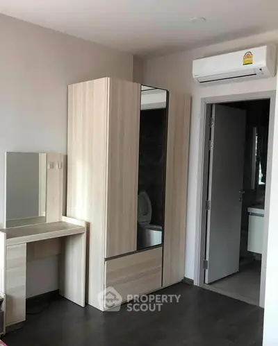 Modern bedroom with sleek wardrobe and vanity, featuring air conditioning and dark wood flooring.