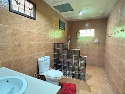 Spacious bathroom with modern shower and tiled walls, featuring a glass block partition for privacy.