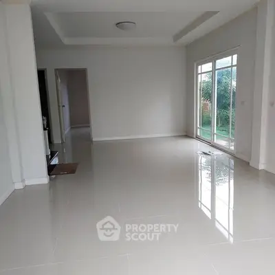 Spacious empty living room with glossy tiled floors and large windows overlooking garden.