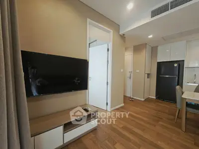 Modern apartment interior with sleek kitchen and cozy living area featuring a wall-mounted TV and wooden flooring.