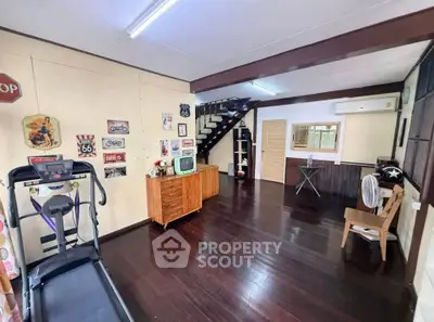 Charming vintage-themed living room with dark wood floors and retro decor, featuring a treadmill and staircase.
