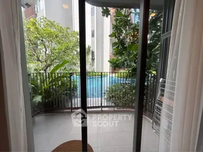 Charming balcony view with lush greenery and pool access in modern apartment complex.