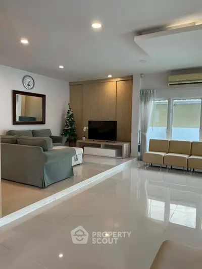 Spacious living room with modern decor and ample seating, featuring a TV and natural light from large windows.