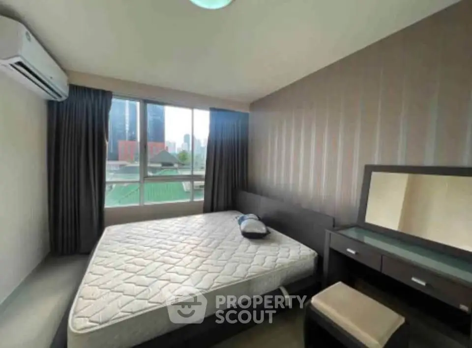 Spacious bedroom with large window and modern furniture in urban apartment.