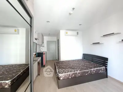 Modern studio apartment with bed, kitchenette, and mirrored wardrobe in a bright, airy space.