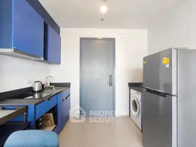 Modern kitchen with blue cabinets, stainless steel fridge, and washing machine in compact layout.