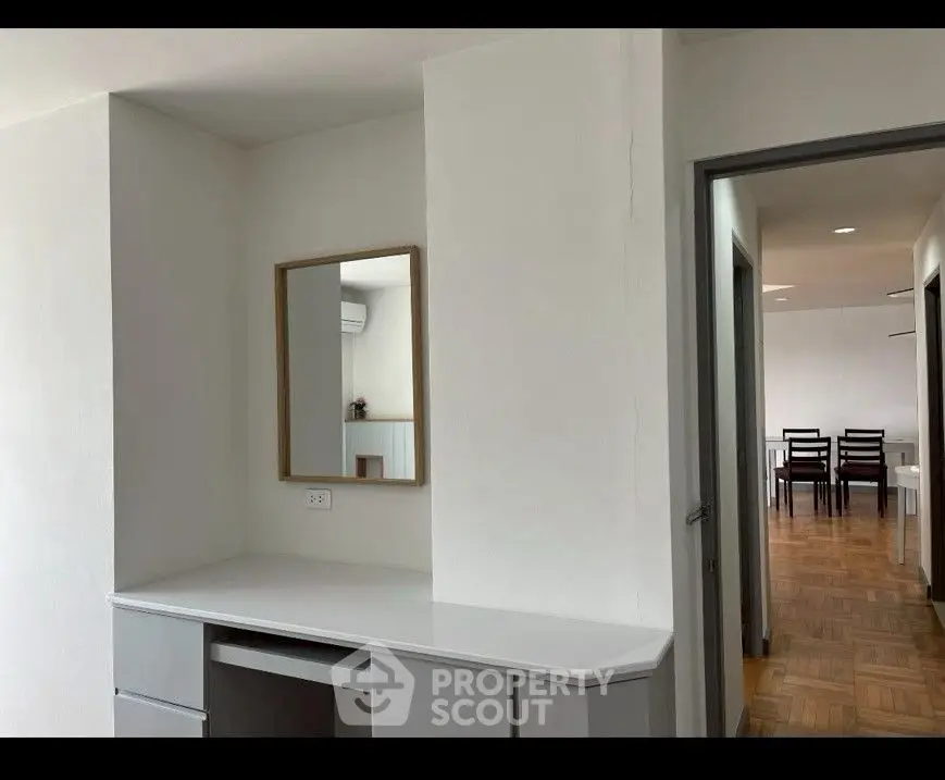 Modern interior with sleek desk and mirror, leading to a dining area with wooden flooring.