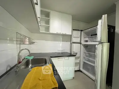 Modern kitchen with sleek white cabinets and open fridge, featuring a double sink and black countertops.