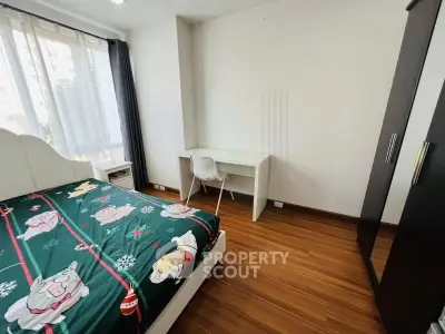 Cozy bedroom with wooden flooring, featuring a bed with colorful bedding, a study desk, and a wardrobe.