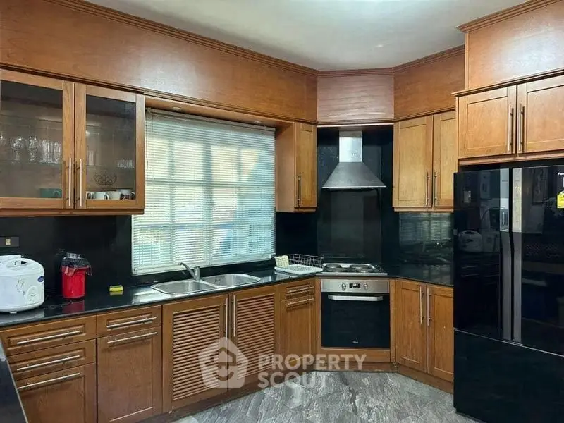Spacious kitchen with modern appliances and wooden cabinetry, featuring a sleek black refrigerator and built-in oven.