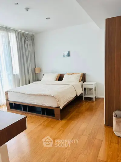 Modern bedroom with wooden flooring and natural light in a stylish apartment.