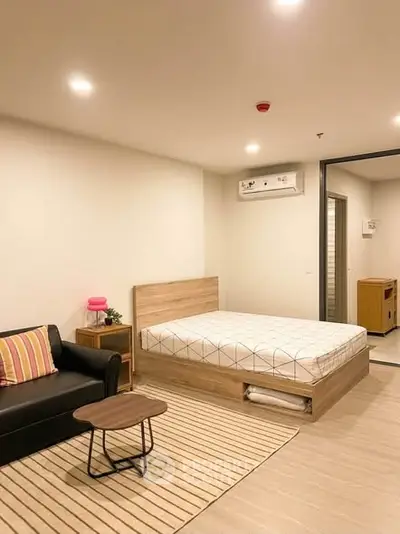 Modern studio apartment with cozy bed, stylish sofa, and sleek wooden flooring.
