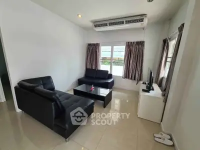 Modern living room with sleek black leather sofas and large windows for natural light.