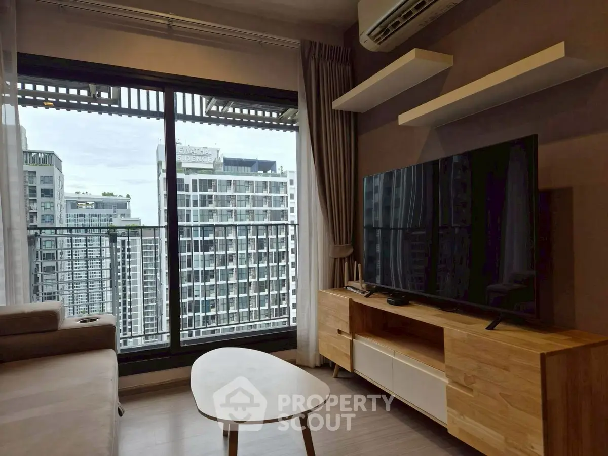 Modern living room with large TV and city view from balcony in high-rise apartment.