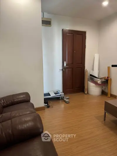 Cozy living room with brown leather sofa and wooden flooring, featuring a modern entrance door.