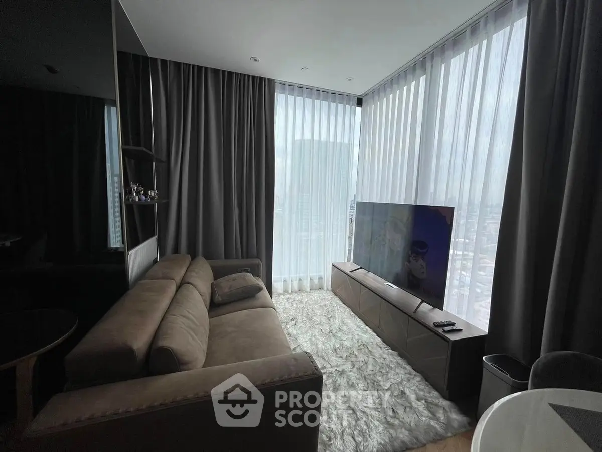 Luxurious living room with plush sofa and large TV, featuring floor-to-ceiling windows and city view.