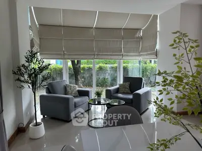 Elegant living room with large windows and modern furniture, offering a serene garden view.