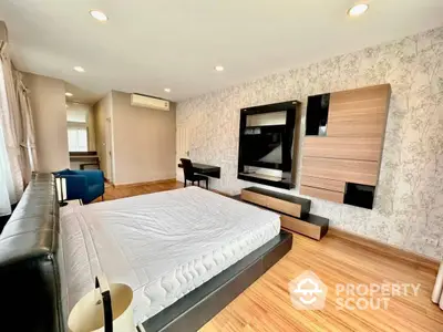 Spacious bedroom with modern wall-mounted entertainment unit, elegant wooden flooring, and ample natural light.