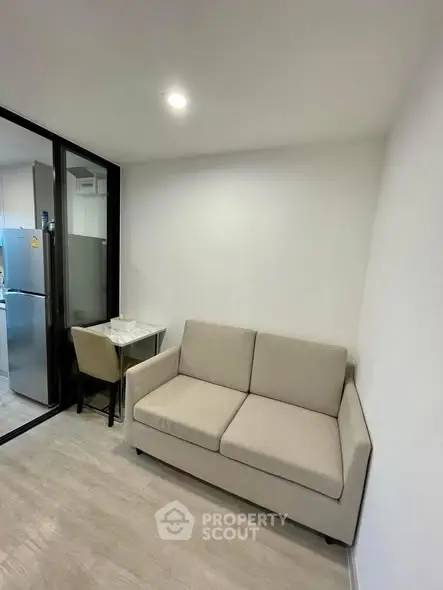 Modern compact living room with beige sofa and glass partition to kitchen