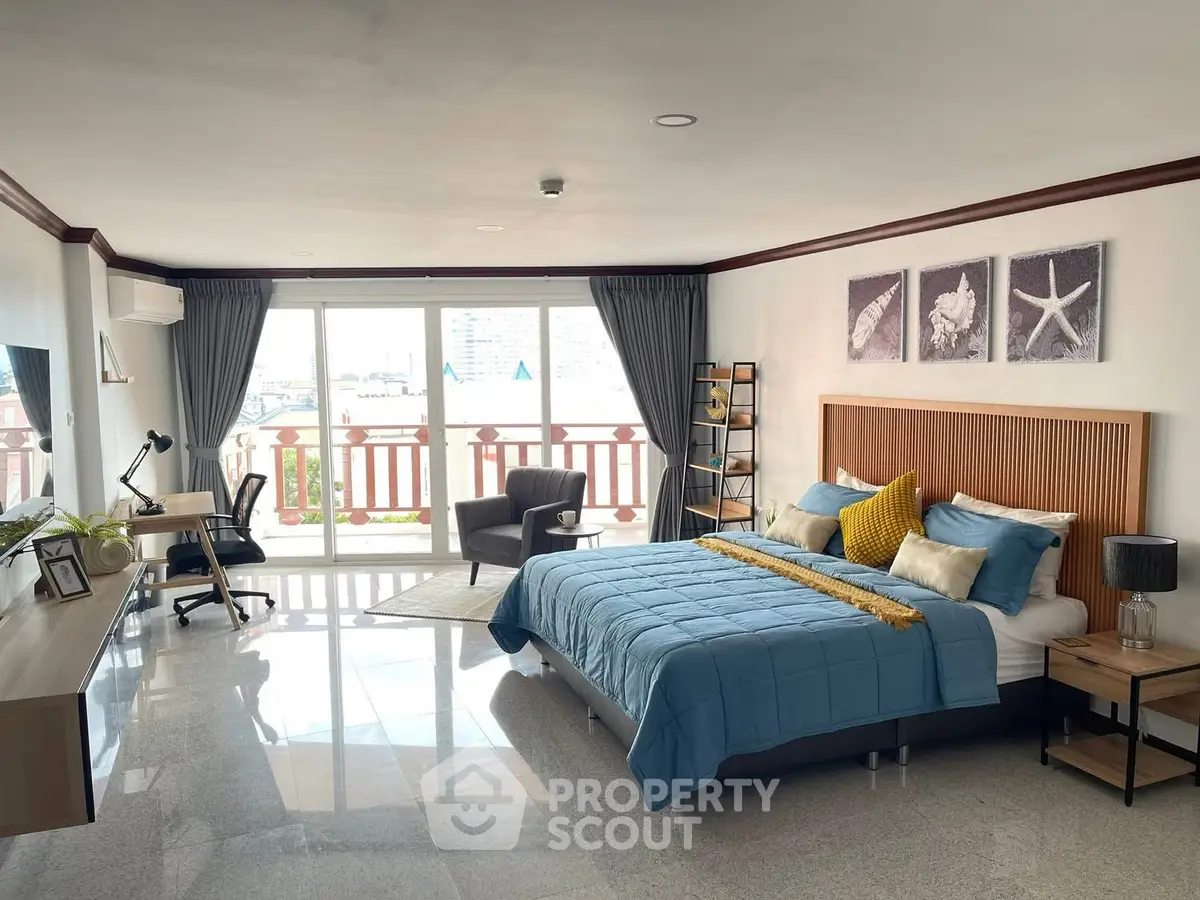 Spacious bedroom with modern decor and balcony view, featuring a cozy workspace and stylish furnishings.