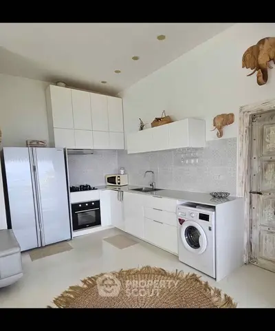 Modern kitchen with sleek white cabinets, built-in oven, and washing machine, featuring elegant decor and bright lighting.