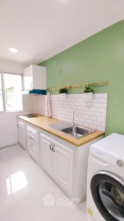 Charming kitchen with white cabinets, wooden countertop, and washing machine in modern apartment.