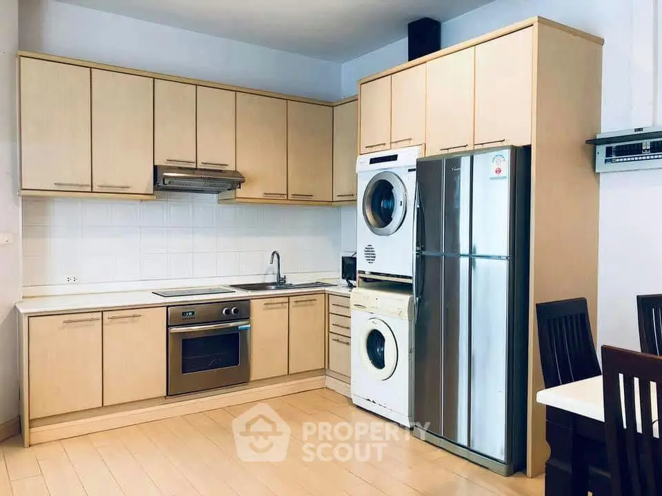 Modern kitchen with wooden cabinets, stainless steel appliances, and in-unit laundry setup.