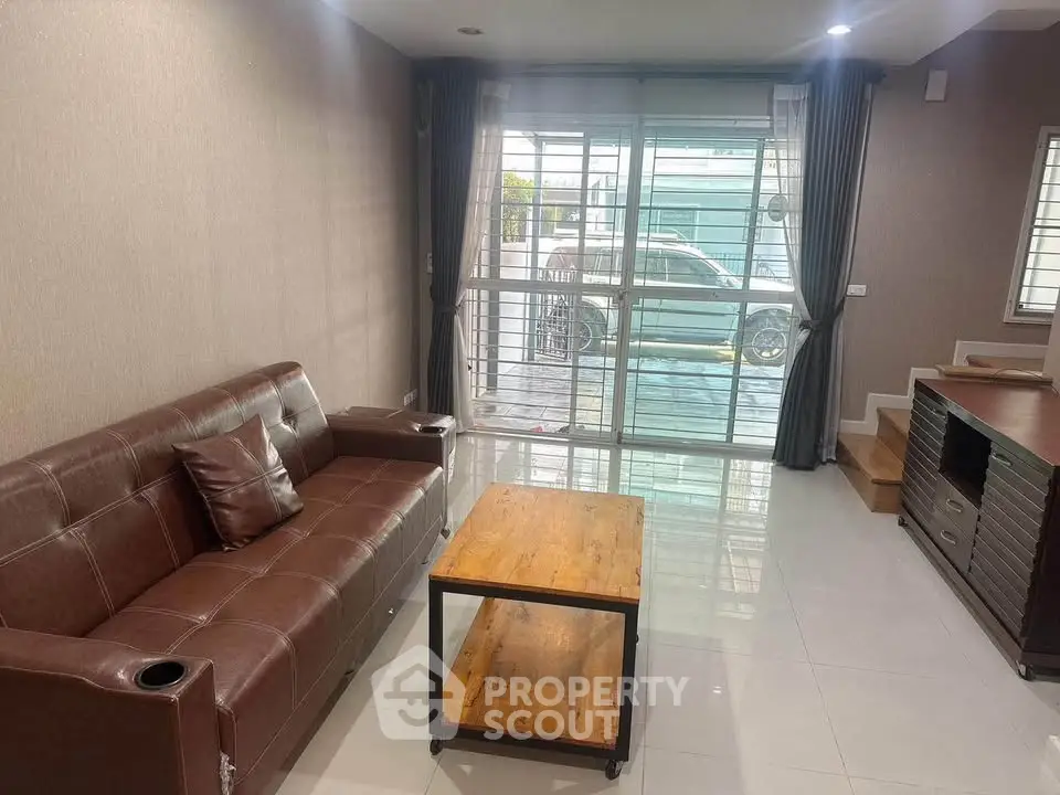 Modern living room with brown leather sofa and wooden coffee table, large windows with curtains.