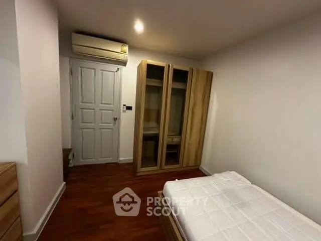 Cozy bedroom with wooden flooring, single bed, and built-in wardrobe, perfect for minimalist living.