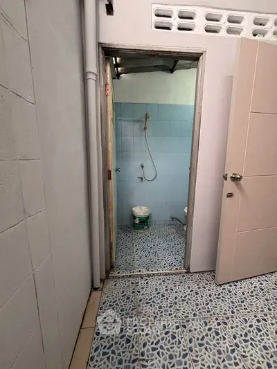 Compact bathroom with blue tiles and shower, featuring a bucket for utility use.