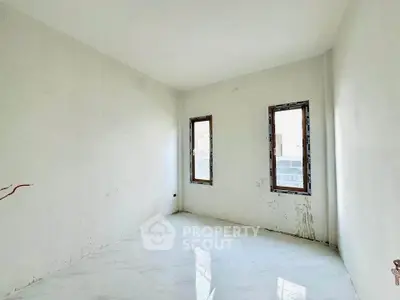Spacious unfinished room with two windows and white walls, ideal for customization.