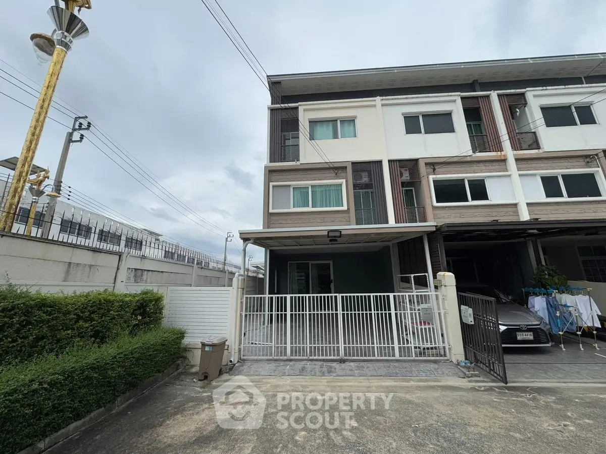 Modern townhouse exterior with gated driveway and adjacent greenery.