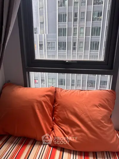 Cozy bedroom with vibrant orange pillows and city view from window.