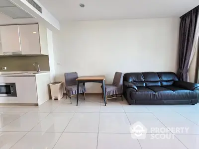 Spacious open-plan living area with sleek tiled flooring, comfortable leather sofa, and a modern kitchen equipped with built-in oven.