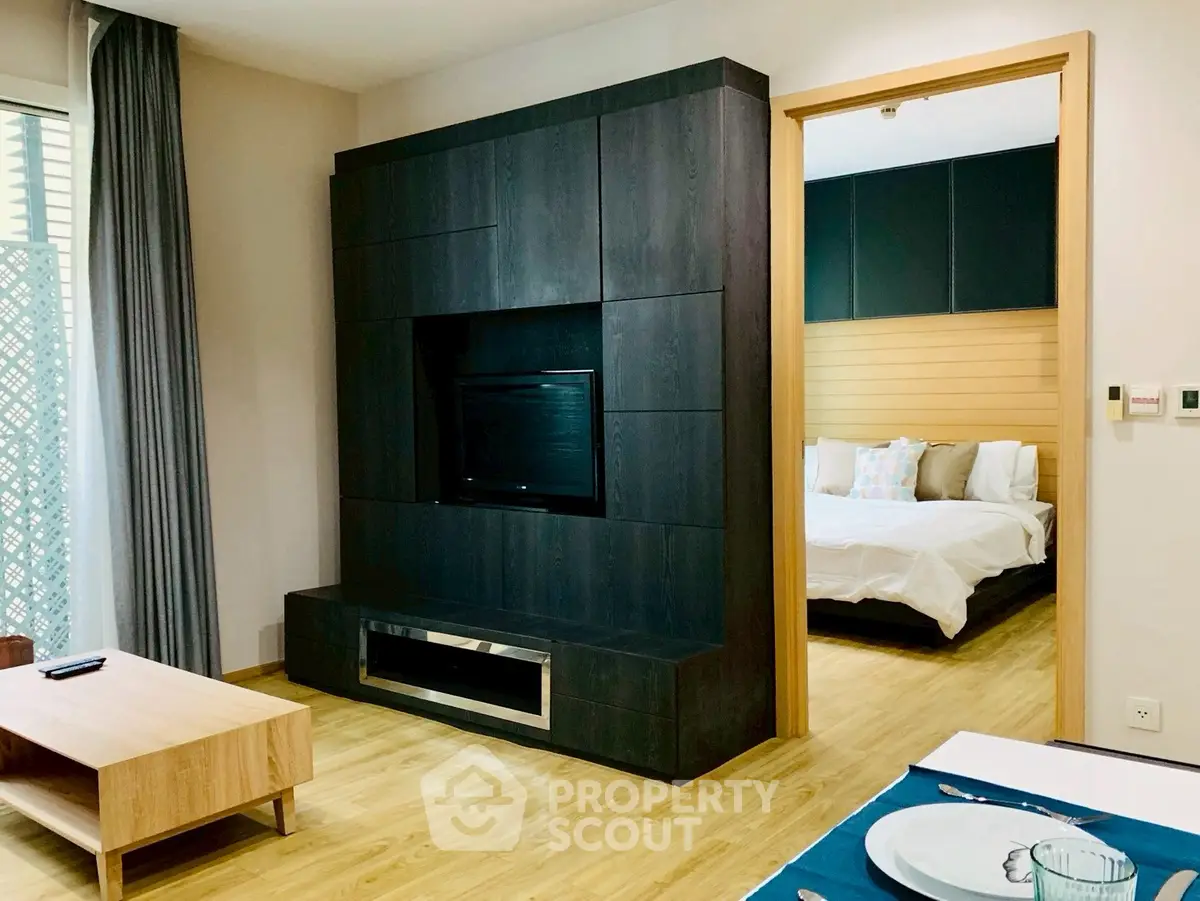 Modern living room with sleek dark wood entertainment center and view into cozy bedroom.
