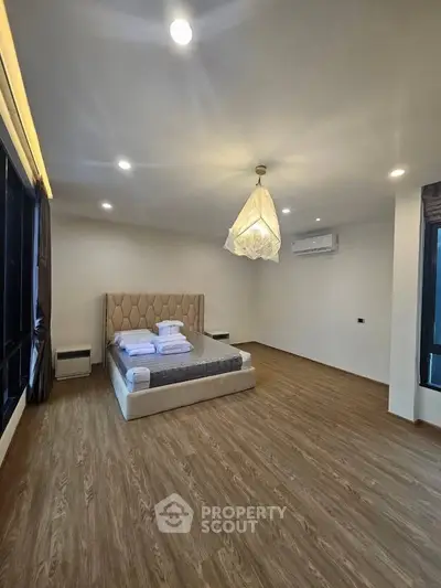 Spacious modern bedroom with elegant lighting and large windows, featuring a stylish bed and wooden flooring.