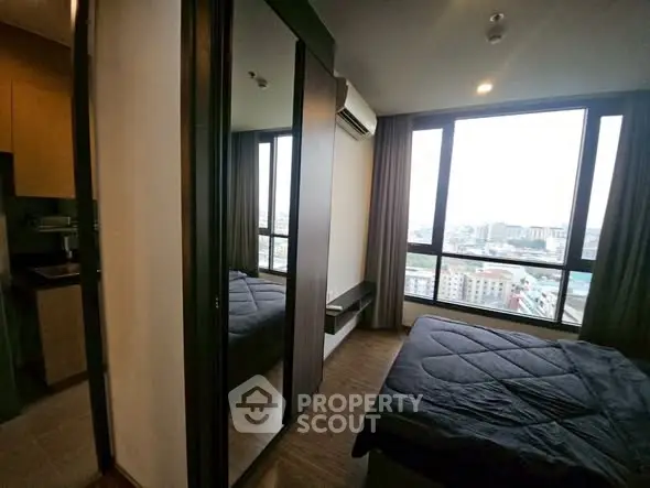 Modern bedroom with large windows offering city views and sleek mirrored wardrobe.