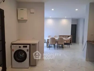 Modern open-plan living area with dining set and washing machine, featuring sleek white interiors.