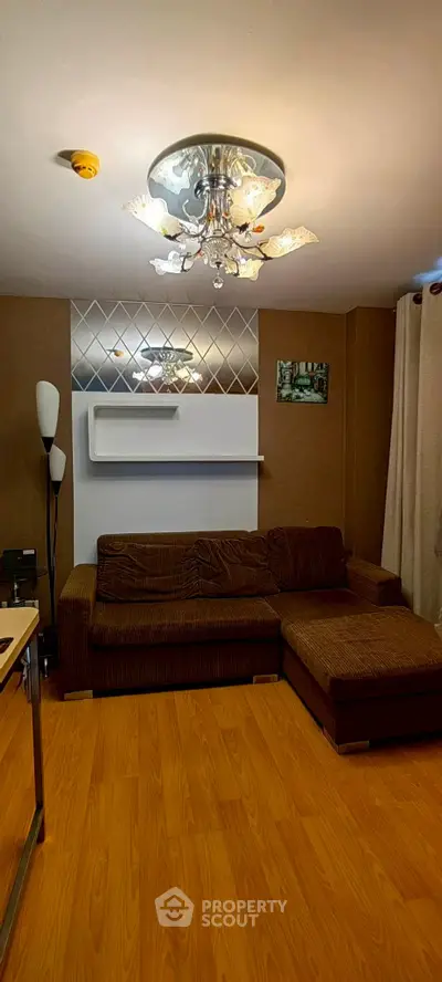 Stylish living room with modern chandelier and cozy brown sofa on wooden flooring.