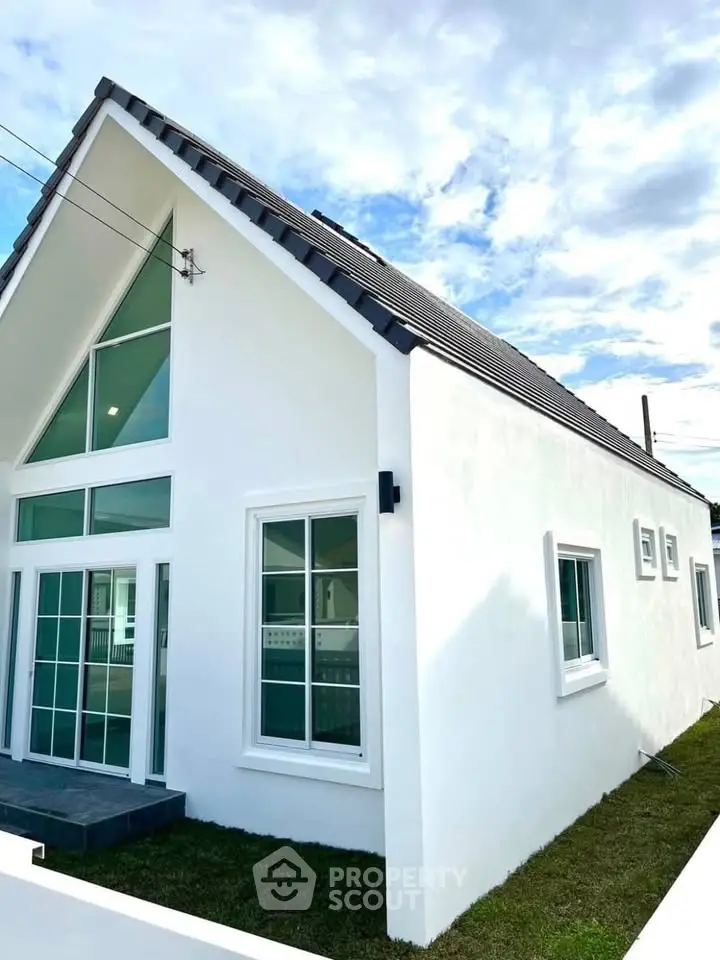 Modern white house with large windows and sloped roof under a clear blue sky.