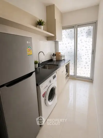 Modern kitchen with sleek appliances and natural light, featuring a washing machine and fridge.