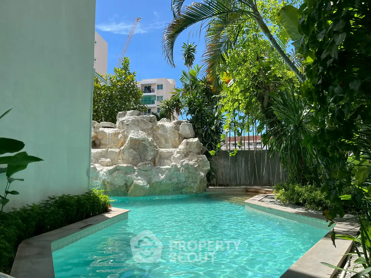Luxurious outdoor pool with lush greenery and rock waterfall feature in a tropical setting.