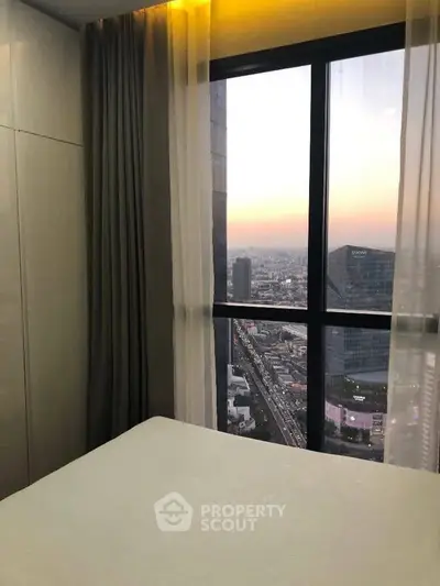 Stunning city view from a modern high-rise bedroom window at sunset.