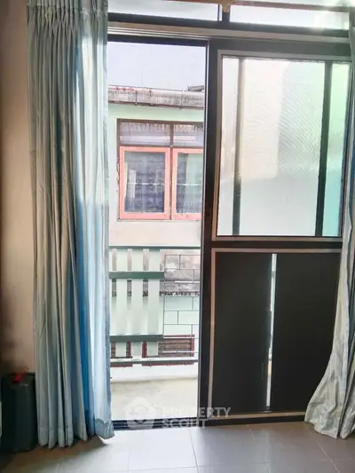 Open balcony door with view of neighboring building, blue curtains, and tiled floor.