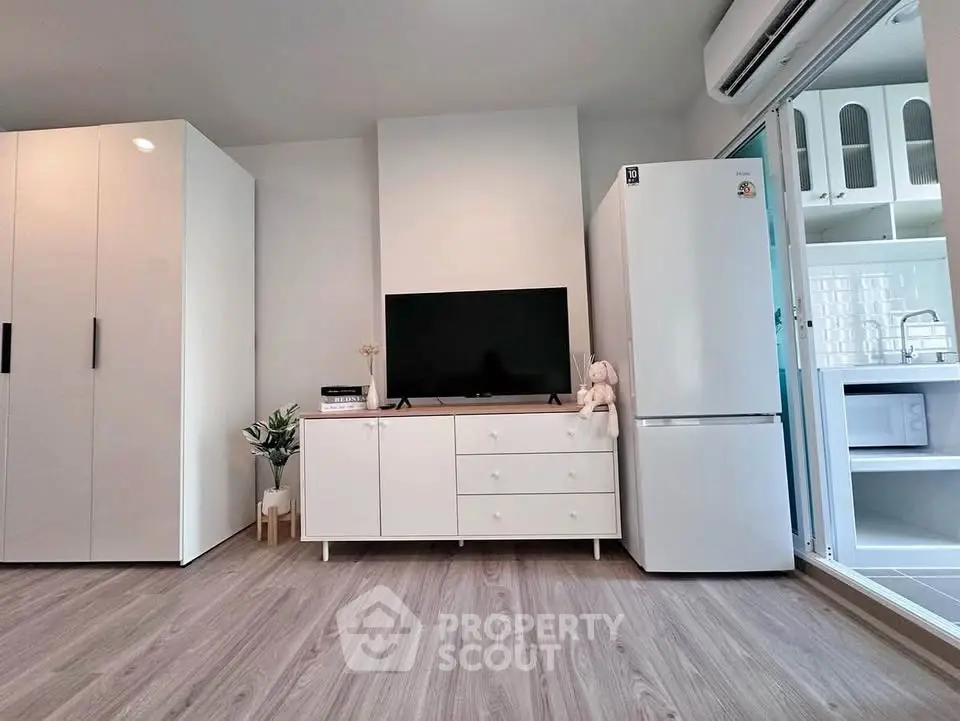 Modern living room with sleek white furniture and appliances, featuring a TV and refrigerator.