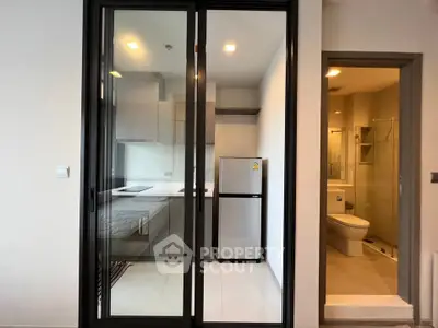 Modern compact kitchen with glass sliding doors and adjacent bathroom in a sleek apartment.