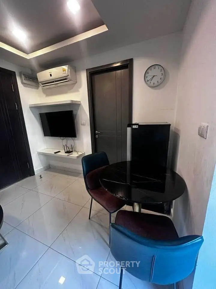 Modern living room with sleek furniture and wall-mounted TV, featuring a compact dining area and air conditioning.