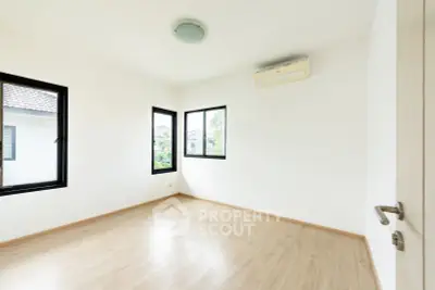 Spacious empty room with wooden flooring and large windows offering natural light.