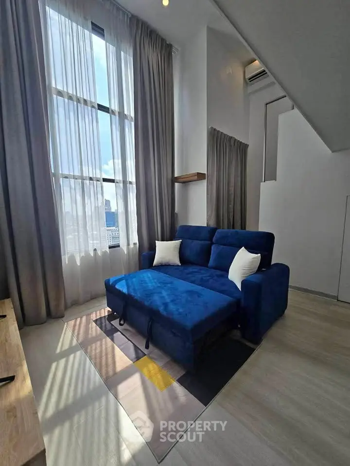 Spacious living room with high ceilings and modern blue sofa, featuring large windows and natural light.