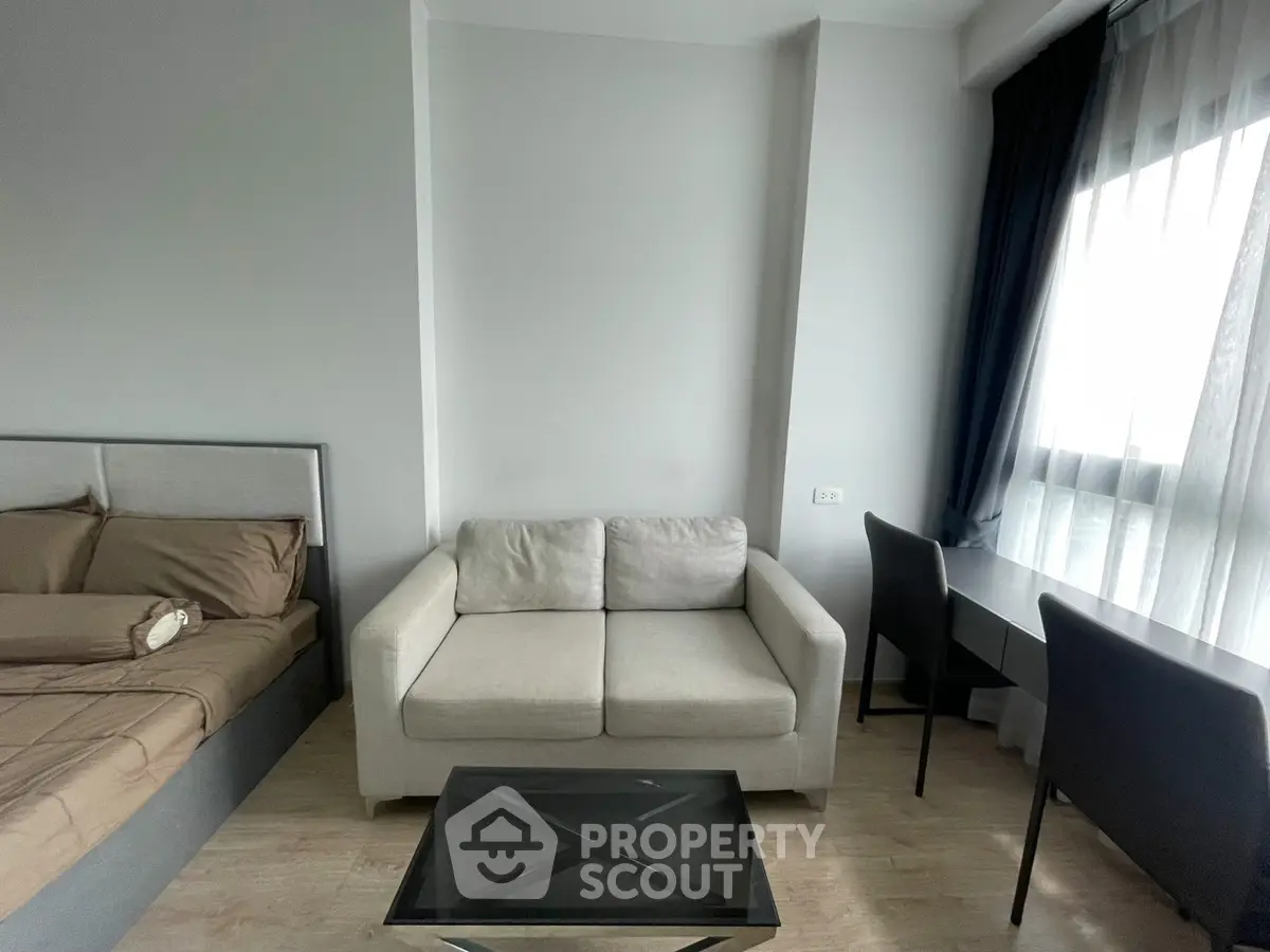 Modern studio apartment with cozy sofa, bed, and natural light from large window.
